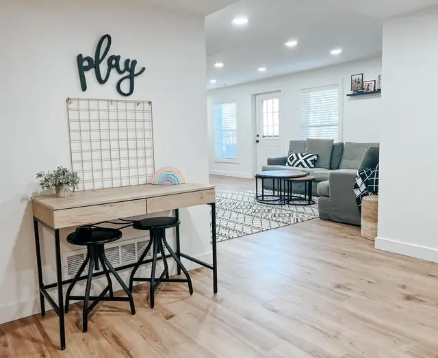 Finished basement playroom with built-in desk, gray sectional and light wood-look floor