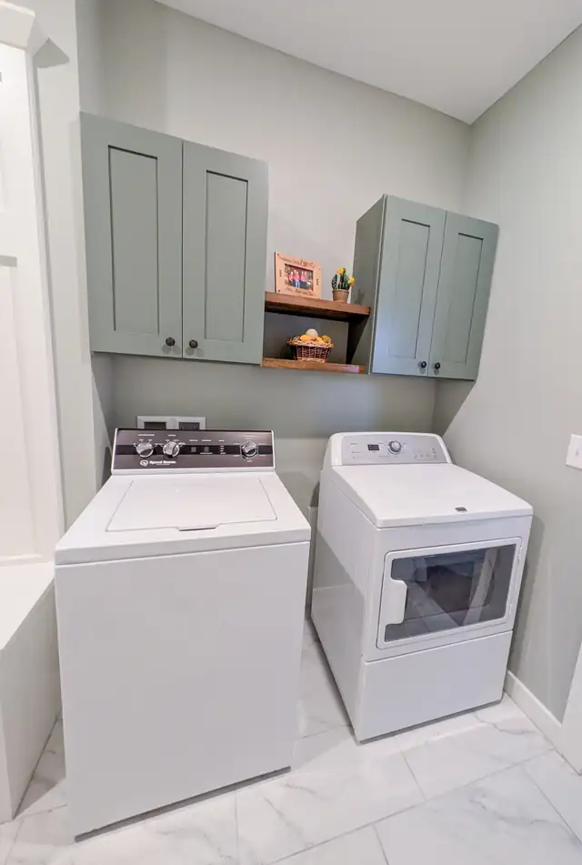 Laundry room remodel in Lee's Summit with sage green upper cabinets, open wood shelf and white washer and dryer