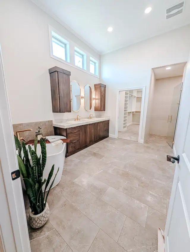 Lee's Summit primary bathroom with dark wood double vanity, high clerestory windows and tile floor leading to an expanded closet
