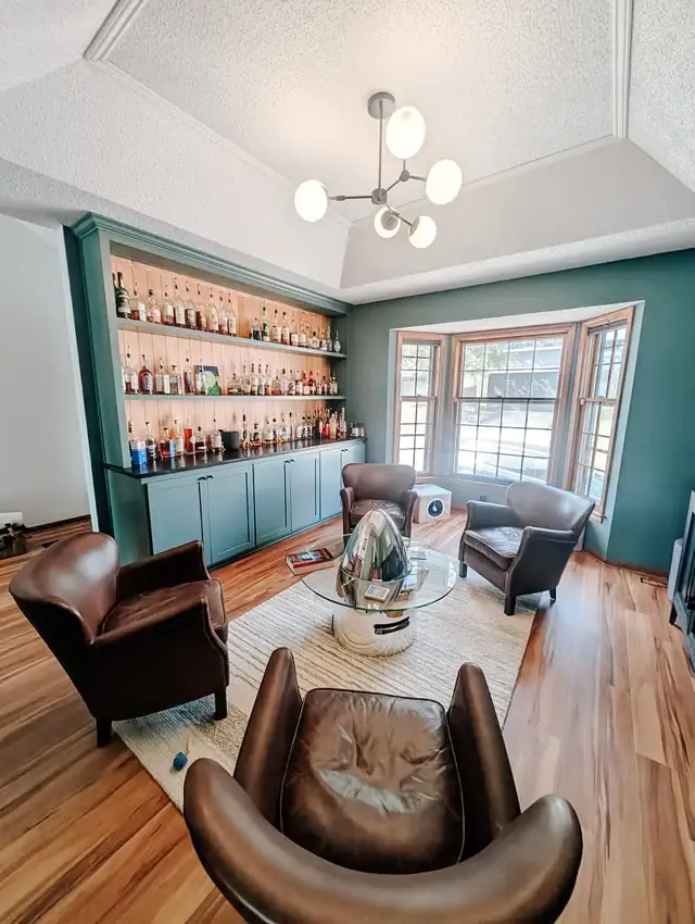 Lee's Summit bourbon room remodel with moody green walls, lit display shelving and leather chairs